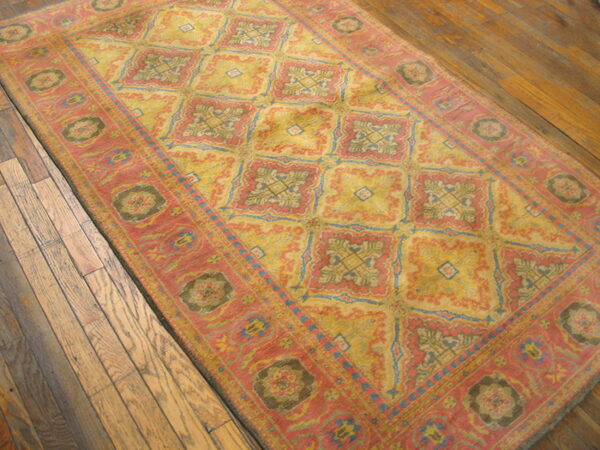 Traditional rug in coral and faded yellow featuring geometric medallions over rustic wood flooring.