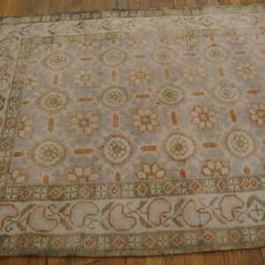 Grayish-blue rug with cream, orange, and green floral and medallion patterns on wood floor.