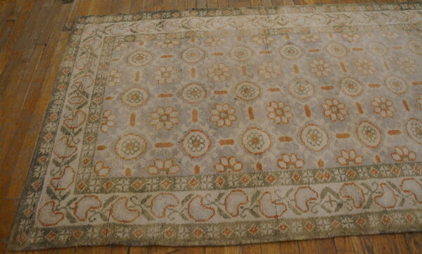 Grayish-blue rug with cream, orange, and green floral and medallion patterns on wood floor.