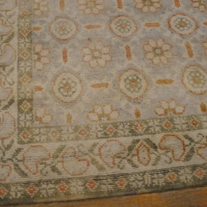 Textured, shaggy rug featuring muted green and peach floral motifs on a beige background over wood plank flooring.