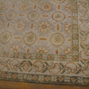 Distressed high-pile rug featuring orange, sage green, and cream floral motifs on hardwood flooring.