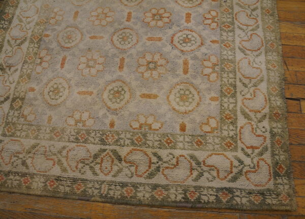 Distressed high-pile rug featuring orange, sage green, and cream floral motifs on hardwood flooring.