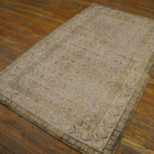 Faded gray rug with repeating floral patterns in soft green and rust colors on rustic wood floor.