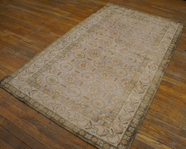 Faded gray rug with repeating floral patterns in soft green and rust colors on rustic wood floor.