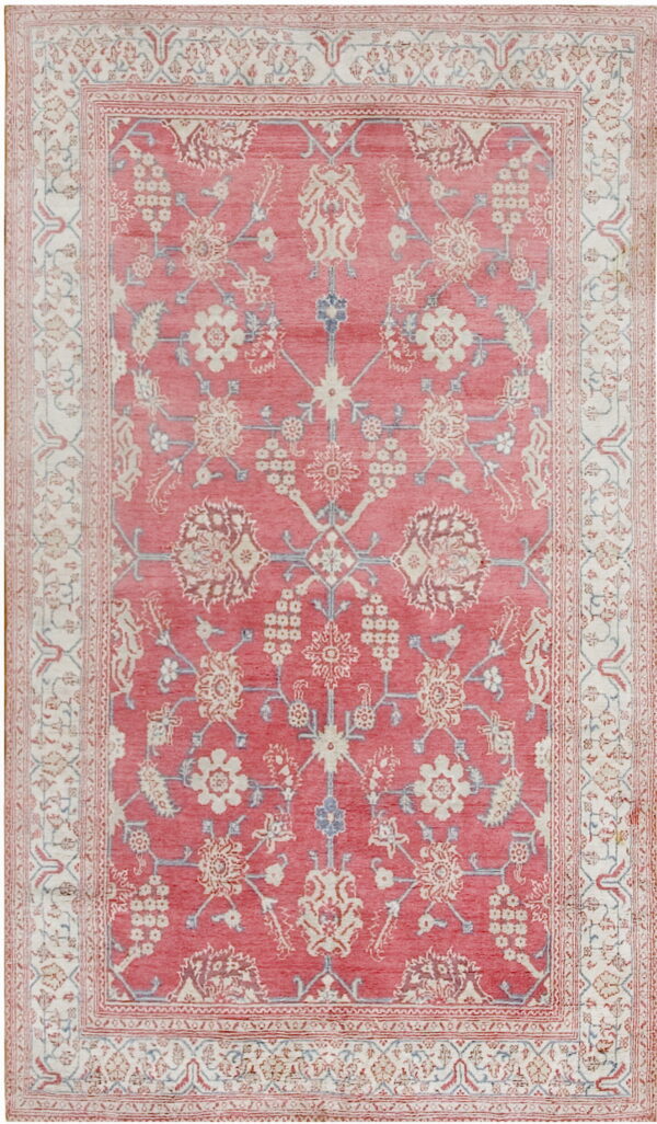 Rectangular low-pile rug featuring a coral field with faded ivory and pale blue intricate floral patterns.