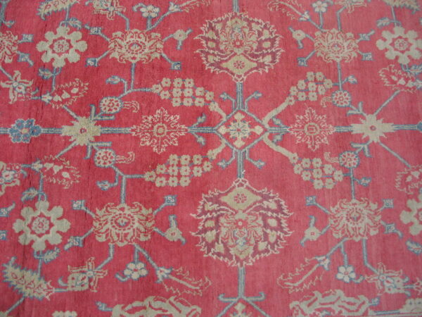 Deep pink rug detail featuring intricate stylized floral patterns in beige, light blue, and burgundy.
