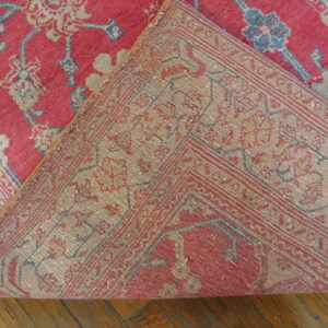 A red, blue, and cream low-pile rug with a floral pattern is folded back to reveal the woven backing.