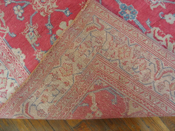 A red, blue, and cream low-pile rug with a floral pattern is folded back to reveal the woven backing.