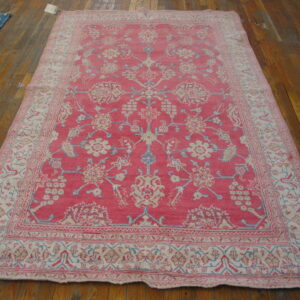Bright pink rug featuring intricate cream and blue botanical patterns on a distressed wood floor.