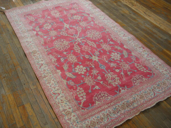 Rectangular pink and cream traditional rug with a detailed floral pattern on wide wood floorboards.
