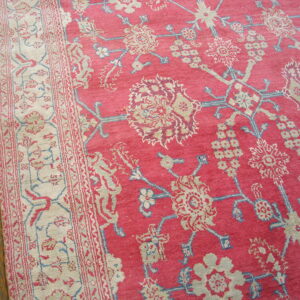 Close-up of a pink floral rug with cream and blue details on a distressed hardwood floor.
