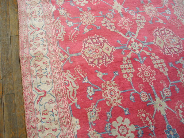 Close-up of a pink floral rug with cream and blue details on a distressed hardwood floor.