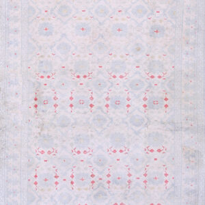 Low pile rug in faded pale blue, pink, and white geometric patterns on distressed wood flooring.