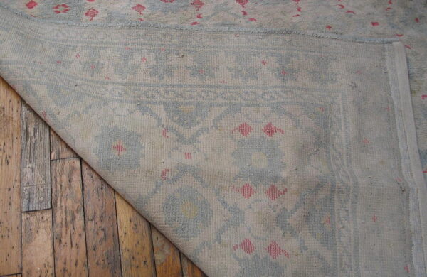 Light blue and beige rug with pink details folded back over distressed wood plank flooring.