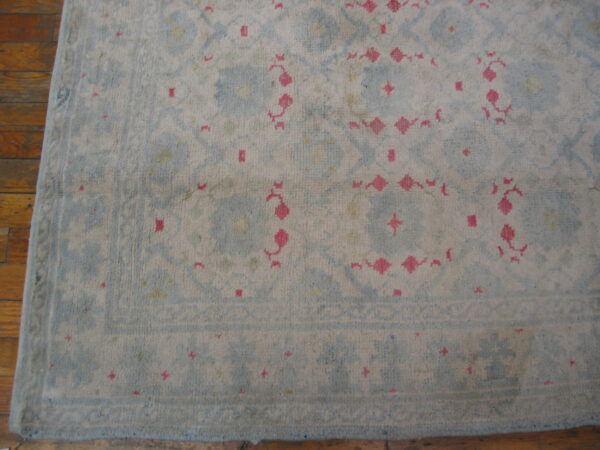 Light blue and cream low-pile rug with pink floral accents and a border rests on brown wood flooring.