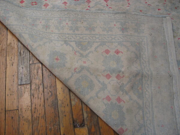 Light beige rug with blue and pink motifs folded back, revealing distressed wood floorboards.