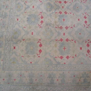 Pale blue and cream rug with distressed traditional pink and geometric motifs on wood floor.
