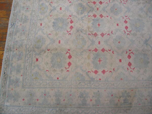 Pale blue and cream rug with distressed traditional pink and geometric motifs on wood floor.