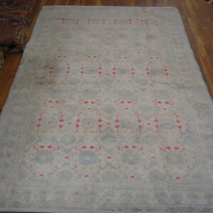 Pale blue and cream rug with repeating pink and geometric patterns rests on a brown wood floor.