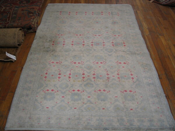 Pale blue and cream rug with repeating pink and geometric patterns rests on a brown wood floor.