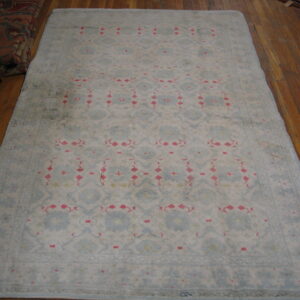 Faded light blue rug with a subtle geometric pattern and bright pink accents displayed on a wood floor.