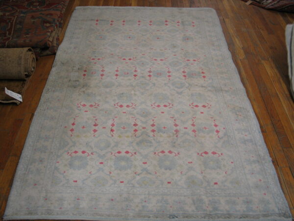 Faded light blue rug with a subtle geometric pattern and bright pink accents displayed on a wood floor.