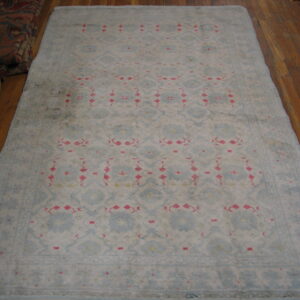 Faded light blue rug with repeating pink and white geometric motifs rests on polished wood floors.