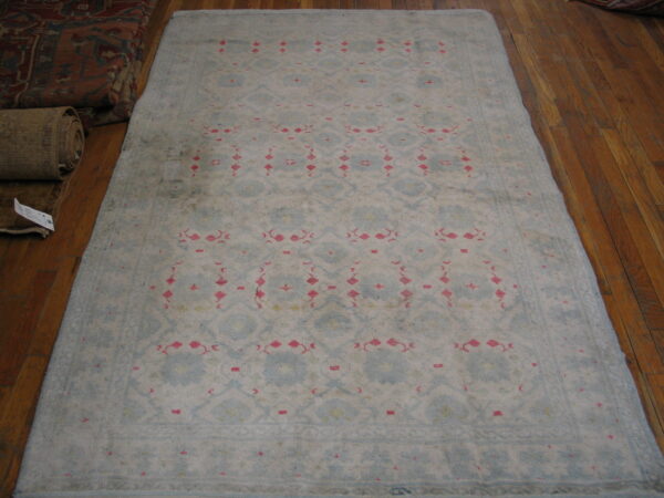Faded light blue rug with repeating pink and white geometric motifs rests on polished wood floors.