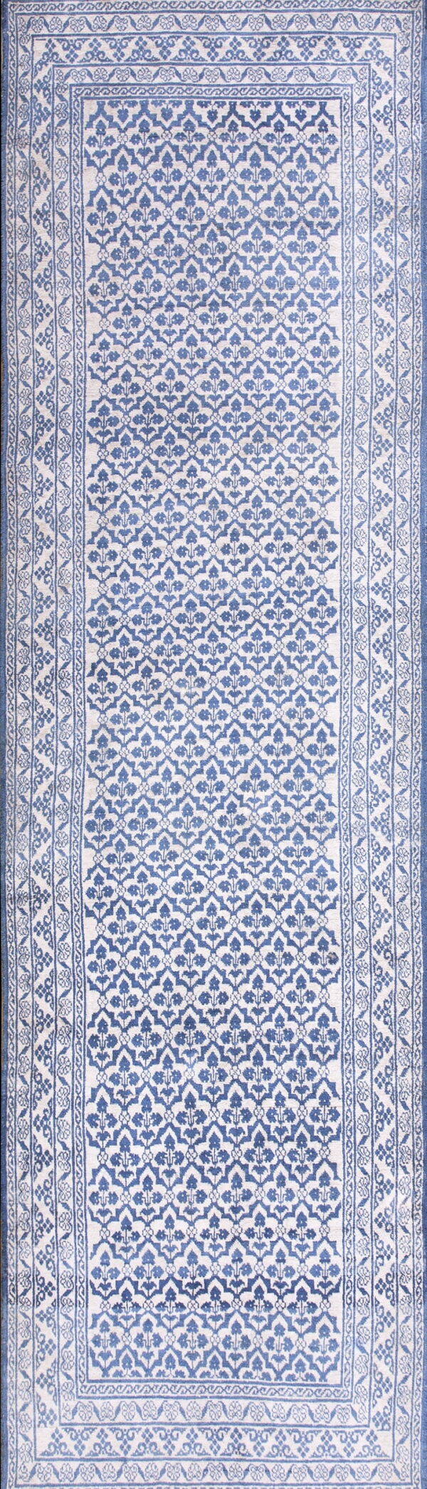 Full view of a blue and cream runner rug featuring an overall trellis design and multiple floral borders.