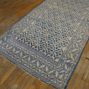A narrow blue and beige runner rug with a detailed border pattern rests on worn rustic floorboards.