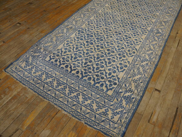 A narrow blue and beige runner rug with a detailed border pattern rests on worn rustic floorboards.