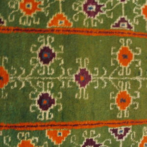 Olive green rug detail features stylized orange and purple geometric motifs and thick orange horizontal bands.