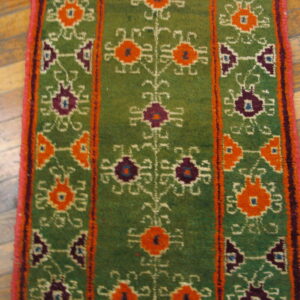 Textured green rug runner featuring colorful orange and dark purple geometric patterns on wood flooring.