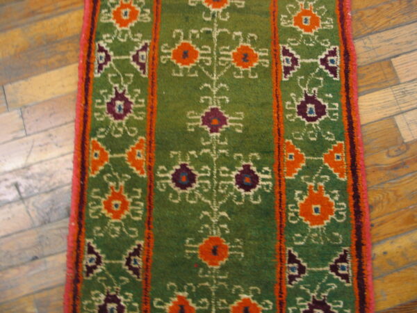 Textured green rug runner featuring colorful orange and dark purple geometric patterns on wood flooring.