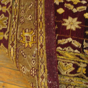 Burgundy and gold patterned rug detail, showing floral motifs and borders over wood plank flooring.