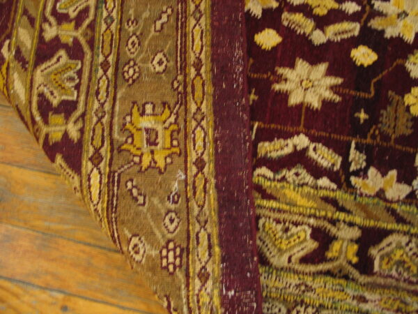 Burgundy and gold patterned rug detail, showing floral motifs and borders over wood plank flooring.