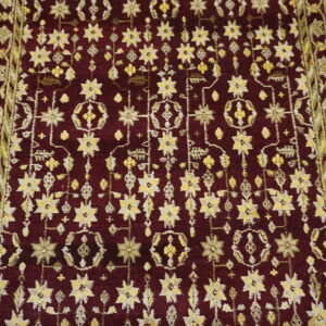 Burgundy rug with dense yellow and cream stylized floral pattern and complex green and gold ornamental borders.
