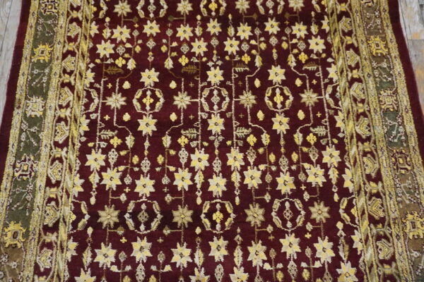 Burgundy rug with dense yellow and cream stylized floral pattern and complex green and gold ornamental borders.