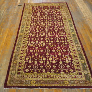 Low-pile rectangular rug featuring yellow star motifs on a crimson field over worn wood flooring.