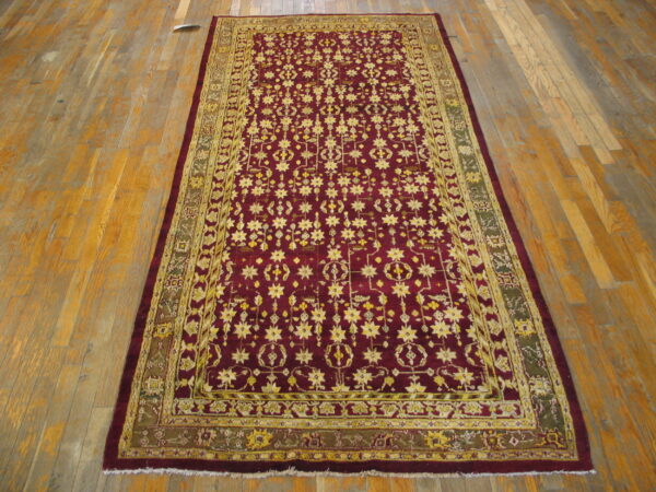 Low-pile rectangular rug featuring yellow star motifs on a crimson field over worn wood flooring.