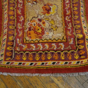 Red and gold floral patterned rug with purple and yellow accents on distressed wood flooring.