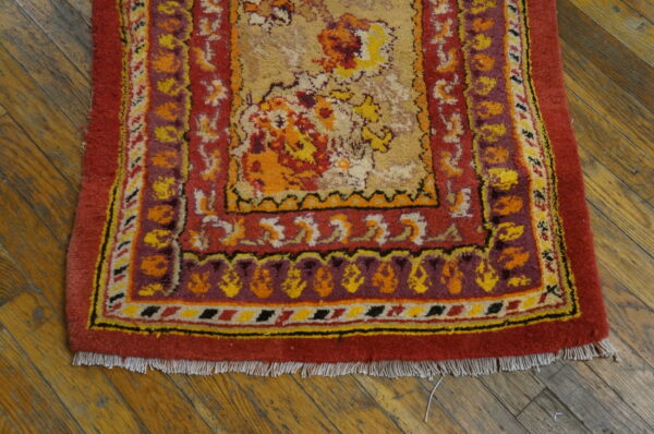 Red and gold floral patterned rug with purple and yellow accents on distressed wood flooring.