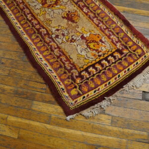Maroon, gold, and orange floral rug runner with fringe resting on weathered wood plank flooring.