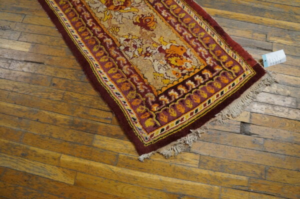 Maroon, gold, and orange floral rug runner with fringe resting on weathered wood plank flooring.