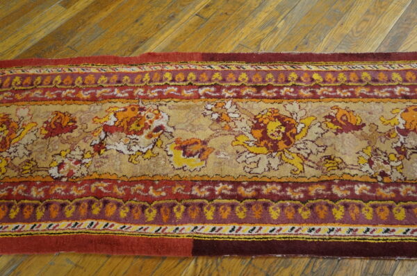 A runner rug with red, gold, and maroon floral and medallion patterns rests on wood flooring.
