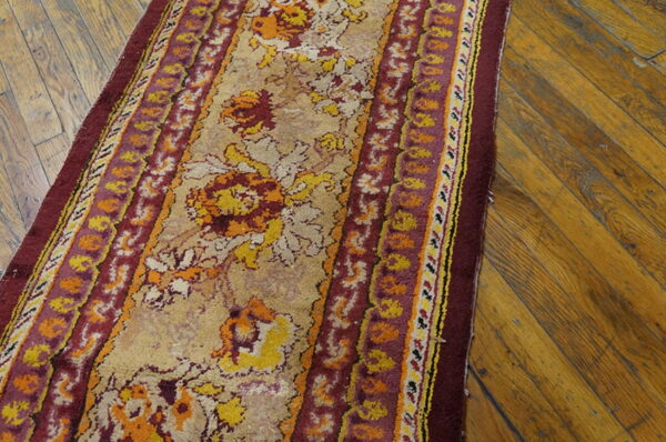 A floral rug runner in burgundy, yellow, and tan rests on worn diagonal hardwood flooring.