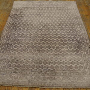 Distressed gray and brown patterned rug with fringe lies on rustic, wide wooden floorboards.