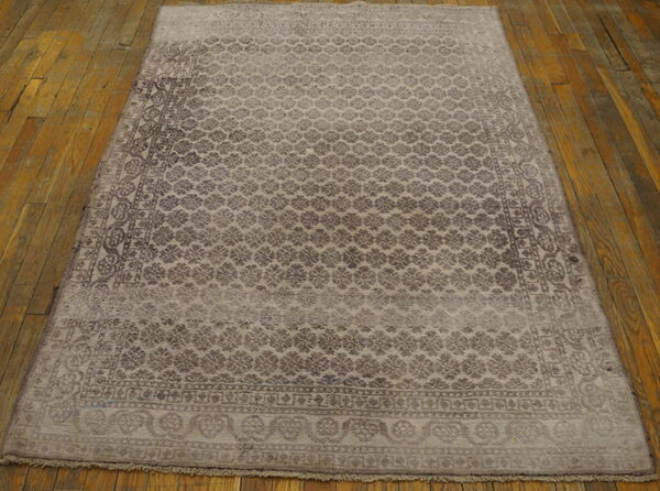 Distressed gray and brown patterned rug with fringe lies on rustic, wide wooden floorboards.