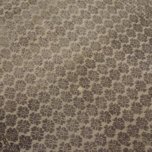 Low-pile taupe rug with repeating dark floral motifs, a patterned border, resting on wood flooring.