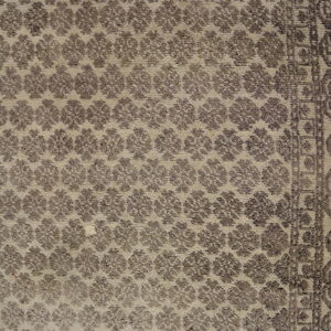 Detail shot of a beige rug patterned with repeating dark taupe floral clusters and a textured border.